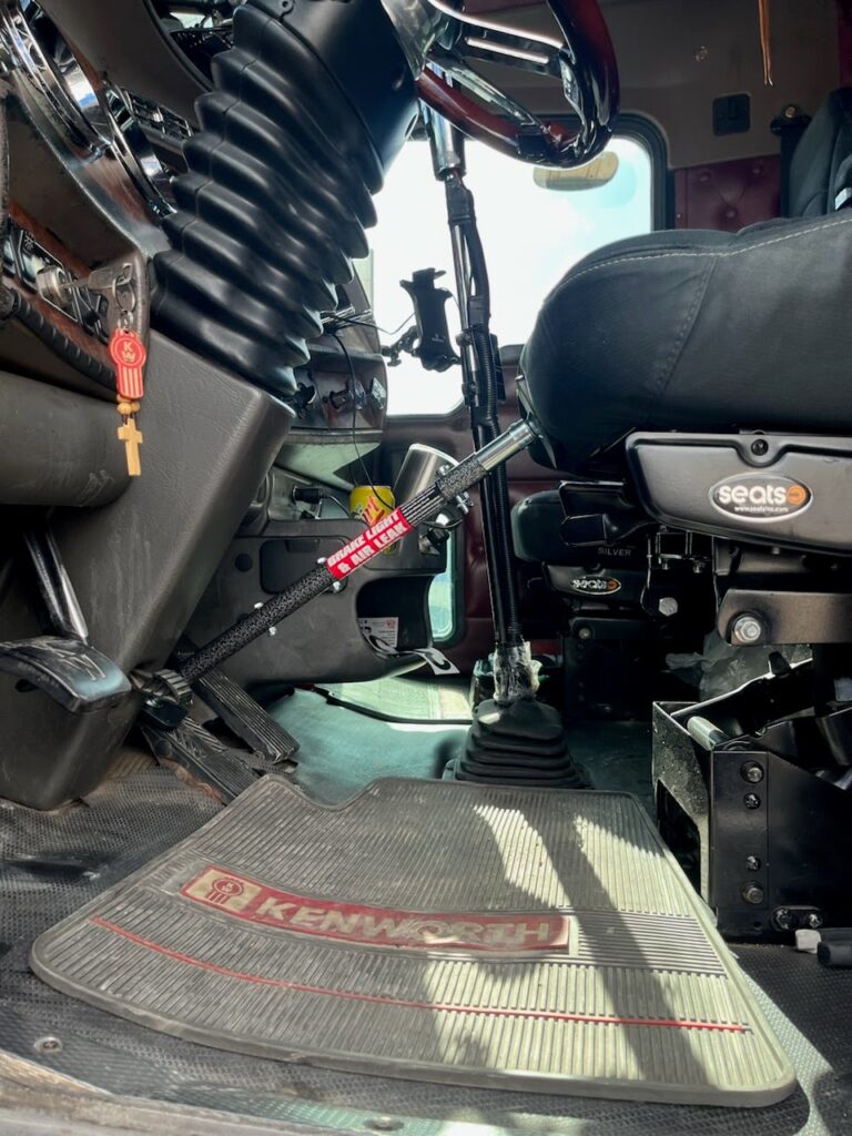 Brake Checker Pro installed between the brake pedal and seat bracket in a Kenworth truck cab